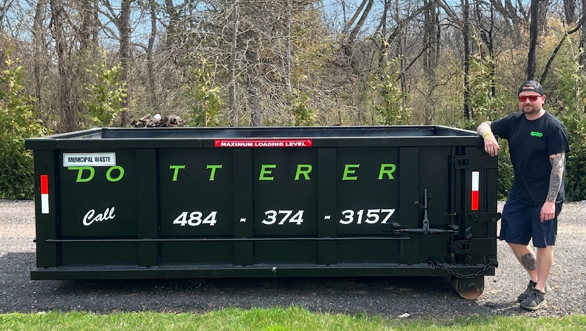 A man next to a Dotterer Disposal dumpster. The dumpster is around the height of the man's chest.