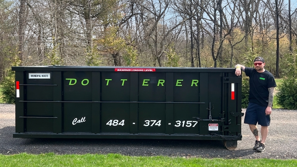 A man next to a Dotterer Disposal dumpster. The dumpster is around the height of the top of the man's shoulders.