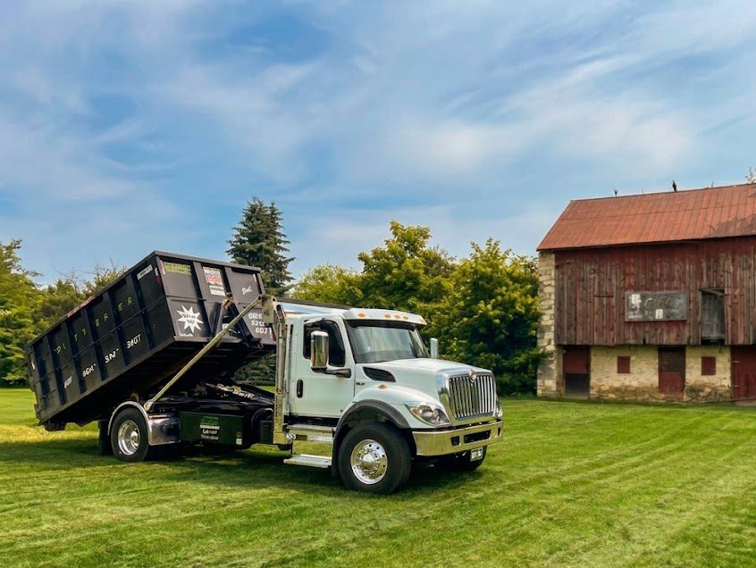 A Dotterer Disposal dumpster truck in front of a barn.