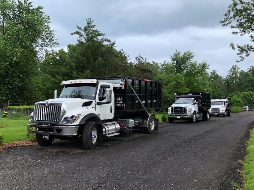 Three Dotterer Disposal dumpster trucks on a road.
