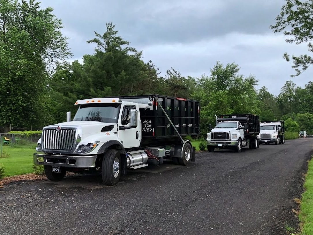 Three Dotterer Disposal dumpster trucks on a road.