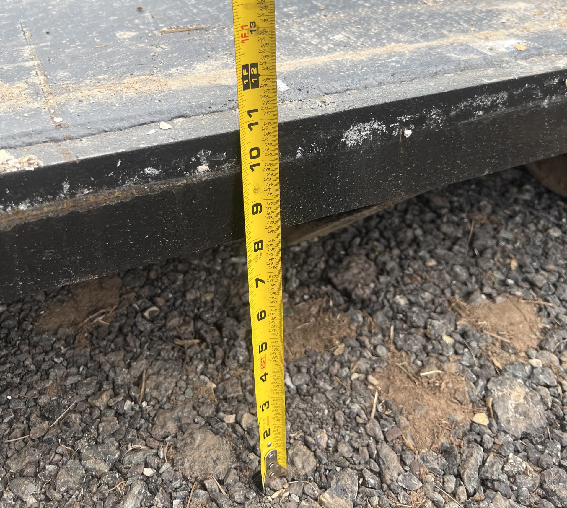 The back end of a dumpster. A tape measure on the ground shows that the top of the dumpster platform is 11 inches off of the ground.