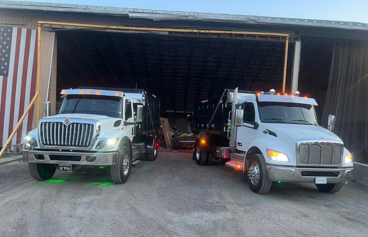 Two Dotterer Disposal trucks in front of a garage